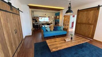 A modern living room with a blue sofa, wooden coffee table, and a hanging light fixture.