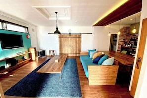Una sala de estar moderna con un televisor grande, muebles de madera y un sofá azul.