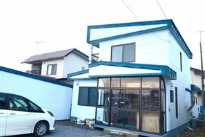 A two-story residential building with a garage and a car parked in front. - Poroto Base (Shiraoi)