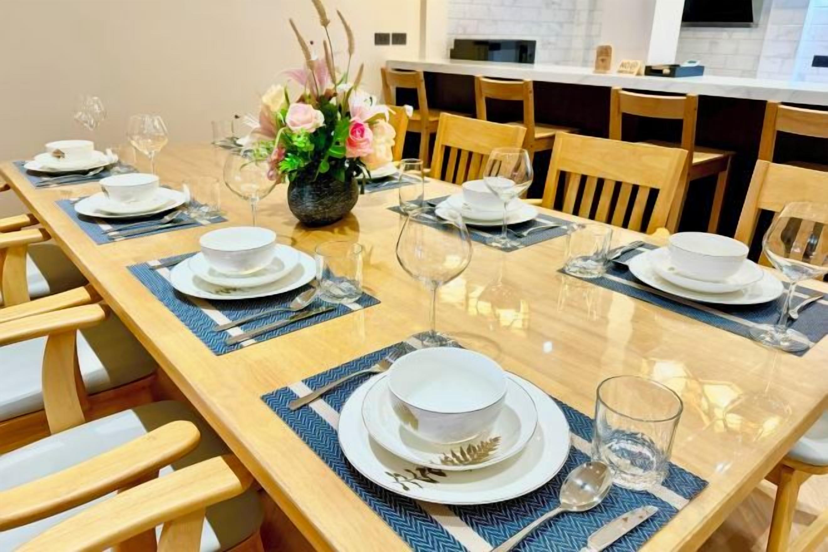 A dining table set with plates, glasses, and cutlery, surrounded by wooden chairs.