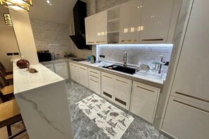 A modern kitchen with white cabinetry, a marble countertop, and a backsplash. - Naka Central Happy Home in Phuket city (Phuket)