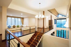 Un intérieur spacieux avec un escalier, un coin salon doté de coussins et de grandes fenêtres.