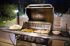 Un barbecue extérieur avec de la nourriture dessus, une assiette remplie de nourriture et un bol contenant de la nourriture.