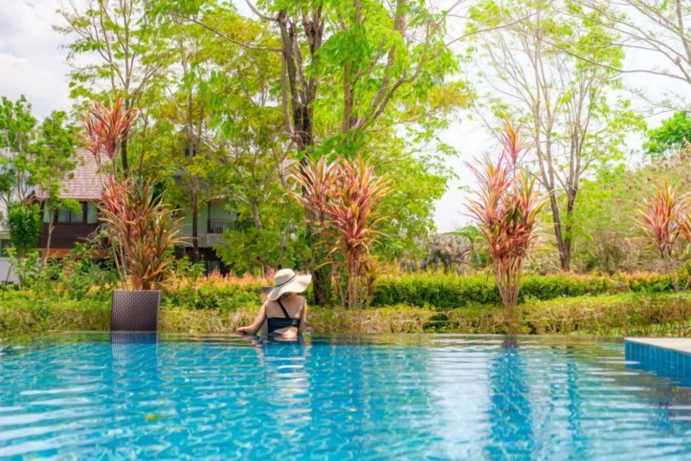 A person in a swimming pool with a view of trees and a building in the background.