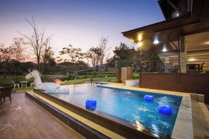 Une piscine extérieure avec un flotteur en forme de licorne, entourée d’une terrasse en bois et d’un espace salon couvert.