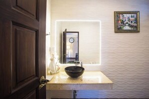 A bathroom with a white textured wall, a black sink, a framed picture, and a wooden door. - Naralin Khaoyai (Pak Chong)