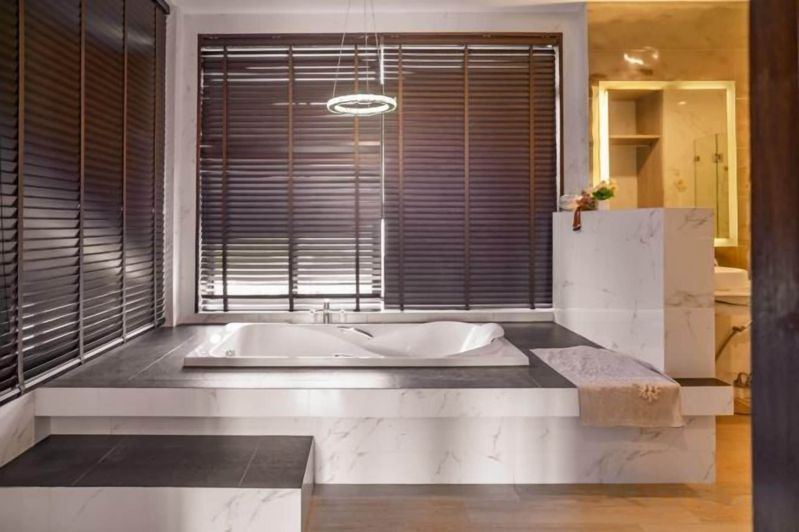 A modern bathroom with a large bathtub, wooden blinds, and a marble countertop.