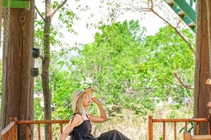 A person sitting on a wooden bench in a covered outdoor area with a view of trees and greenery. - Naralin Khaoyai (Pak Chong)