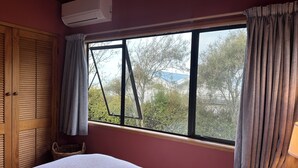 Een slaapkamer met een bed, een raam met gordijnen, een houten kledingkast en een airconditioner.
