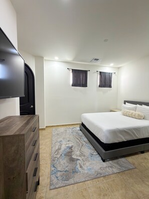 A bedroom with a bed, a TV mounted on the wall, a dresser, and a rug.
