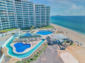 Ein Resort mit mehreren Schwimmbecken, einem Strandbereich und einem großen Hotelgebäude.