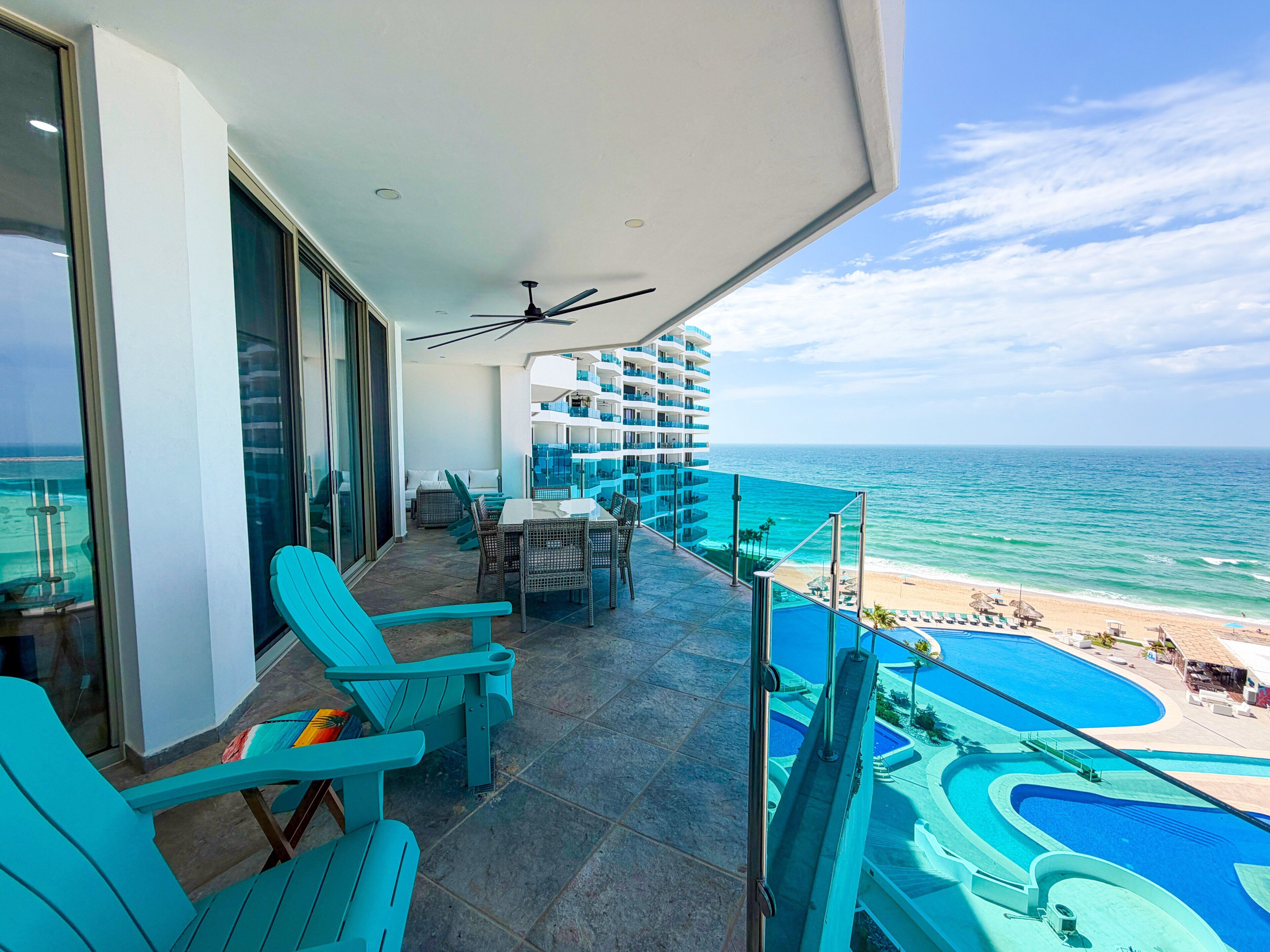 Een balkon met uitzicht op de oceaan, een zwembad en een eethoek met stoelen en tafels.