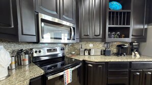 A kitchen with dark cabinetry, a stainless steel microwave, a gas stove, a toaster, and a coffee maker. - Esmeralda Beach Resort 3 Bedrooms C 703 (Puerto Peñasco)