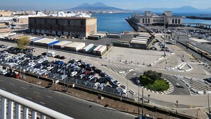 A coastal cityscape with a large port, a prominent building with a dome, and a mountain in the distance. - Mia Suites Angioino (Naples)