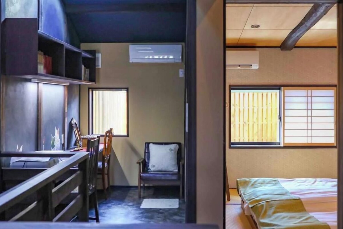 A room with a desk, chair, bed, and a window with blinds.