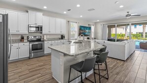 Una cocina moderna con gabinetes blancos, electrodomésticos de acero inoxidable y una isla de granito con taburetes de bar.