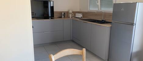 A modern kitchen with grey cabinets, a stainless steel refrigerator, a built-in oven, and a window with blinds.