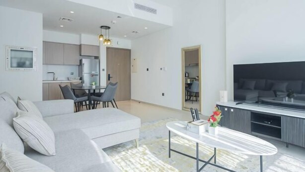 Un salón moderno con sofá, una mesa de centro y televisor. Cuenta con un comedor con sillas y una mesa. El ambiente tiene techos altos con iluminación empotrada.