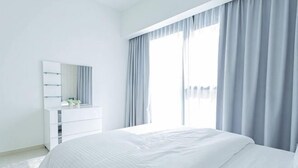 Un dormitorio moderno con una cama grande, un tocador blanco y una ventana con cortinas.
