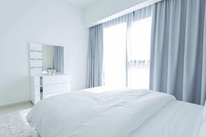 A modern bedroom with a large bed, a white dresser, and a window with curtains. - MH- Act – Downtown 1BHK-REF4006 (Dubai)
