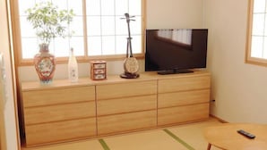 Una habitación con un armario de madera, un televisor, un florero con una planta y una mesita con un control remoto.