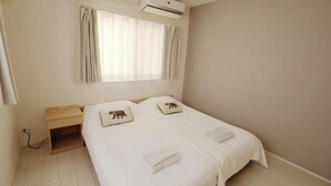 Una cama individual con cabecera, una mesita de noche, una ventana con cortinas y un equipo de aire acondicionado.
