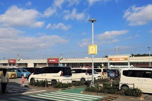 A parking lot with multiple vehicles, a pedestrian crossing, and a building with signage in a foreign language. - 15 Minutes to Airport~1 Minute Walk to Beach YeHeJu (Itoman)