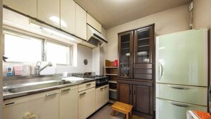 A compact kitchen with white cabinets, a stainless steel sink, a two-door refrigerator, and a small wooden stool. - Higashi Mukojima 4 Room (Tokyo)