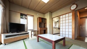 A traditional Japanese-style room with tatami flooring, a television on a wooden cabinet, a dining table, and sliding doors. - Higashi Mukojima 4 Room (Tokyo)