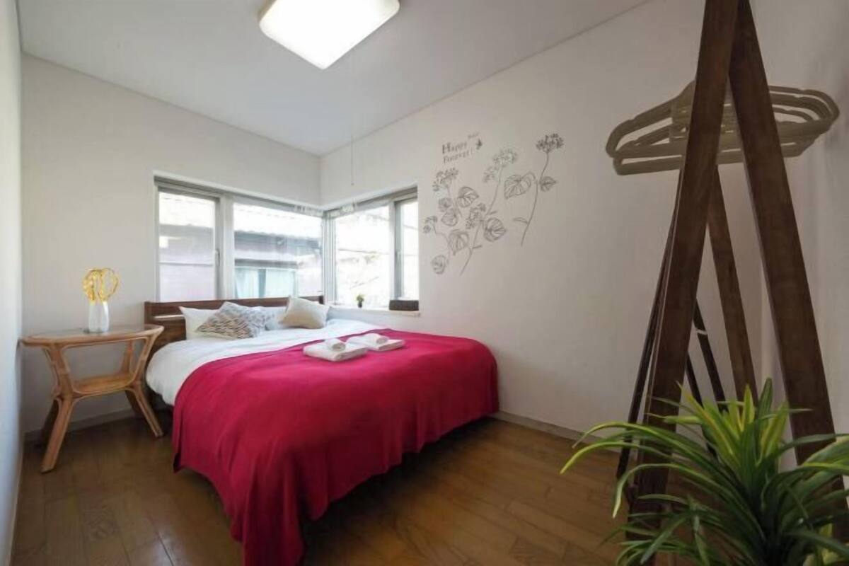 A bedroom with a bed, a window, a wall decoration, a wooden ladder, and a plant.