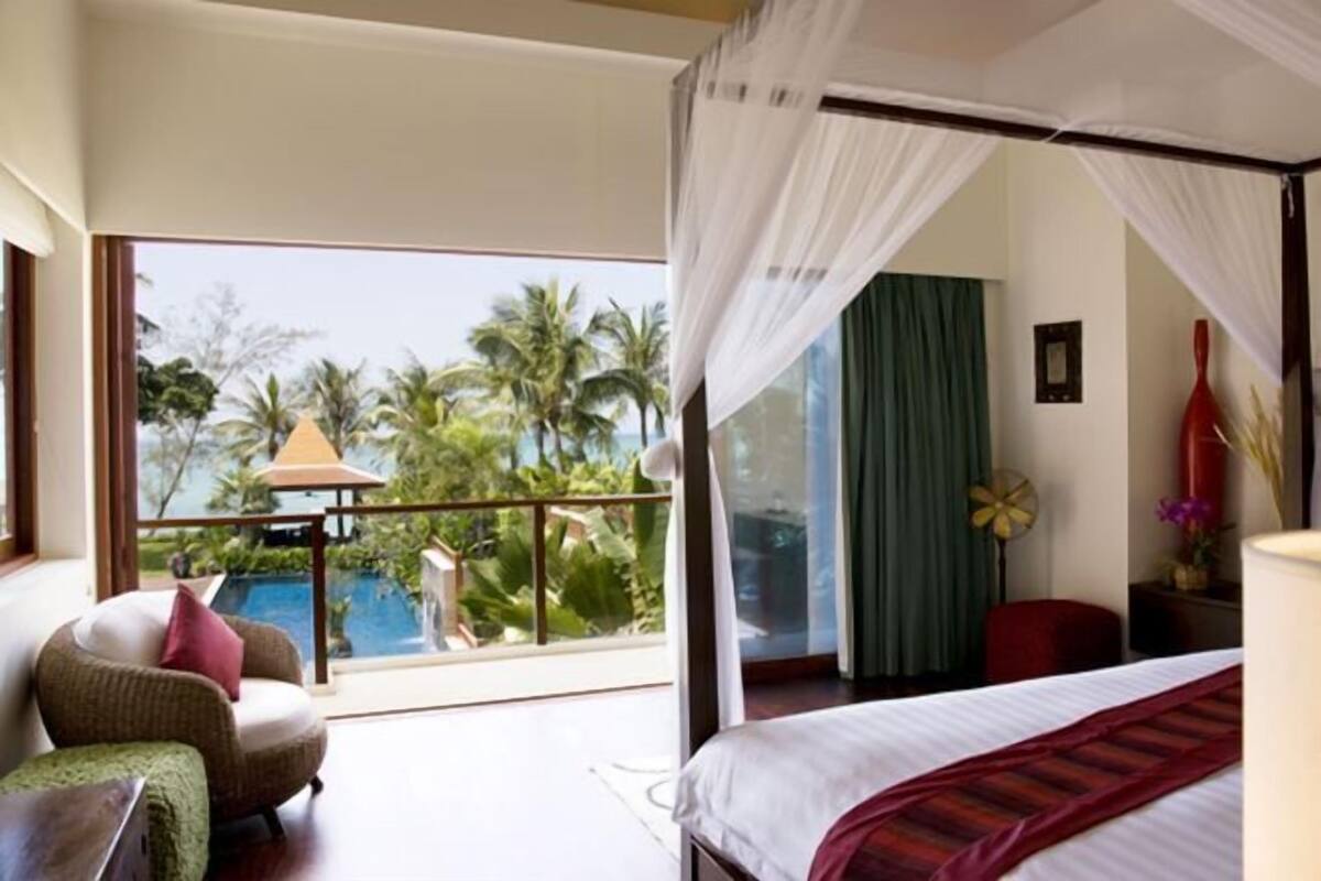 A bedroom with a large window, a bed, a chair, and a nightstand.