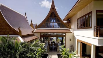 Um edifício tradicional em estilo tailandês com um pátio central, uma área de estar coberta e uma escadaria que dá acesso aos andares superiores.