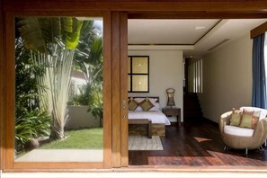 A room with a bed, a chair, a bedside table, and a view of a garden.