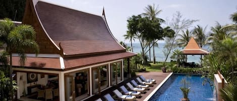 A resort with a pool, lounge chairs, and a traditional building with a sloped roof.