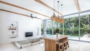 A modern kitchen with a wooden island, built-in shelves, and a large window overlooking a garden. - ULU 5 ·2br Villa (Bali)
