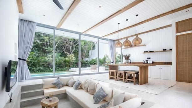 A modern living room with a sofa, a dining table, and a kitchen area with wooden cabinets and pendant lights. - ULU 5 ·2br Villa (Bali)