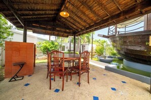 An outdoor dining area with a table and chairs, a large ship model, and a covered roof structure. - Royal Boat Pool Villa - Pattaya (Pattaya)