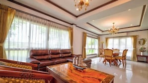 A spacious living room with a leather sofa, a wooden coffee table, and a dining area with a chandelier. - Royal Boat Pool Villa - Pattaya (Pattaya)