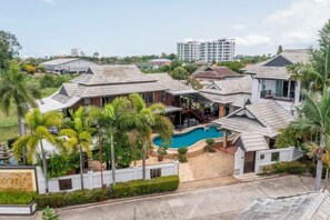 A residential area with multiple houses, a swimming pool, and a large building in the background. - Royal Boat Pool Villa - Pattaya (Pattaya)