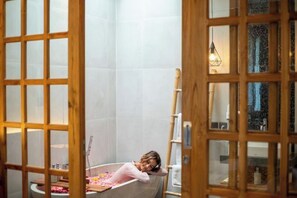 A bathroom with a bathtub, a wooden door, and a towel rack. - Kairos Villa Ubud (Bali)