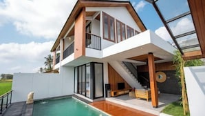 A modern two-story house with a large glass balcony, a swimming pool, and a staircase leading to the upper floor. - Kairos Villa Ubud (Bali)