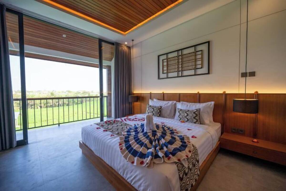 A modern hotel room with a large bed, a wooden ceiling, and a view of a green landscape through large windows.