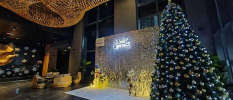 Um hall de entrada com uma grande árvore de Natal, uma mesa de recepção e uma parede com uma placa.