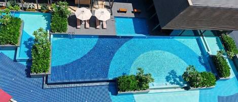 A rooftop swimming pool with lounge chairs and umbrellas, surrounded by greenery and modern architecture.