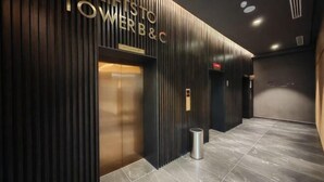 Un área de ascensor moderna con un cartel que indica “TOWER B&C” y un botón de elevador.