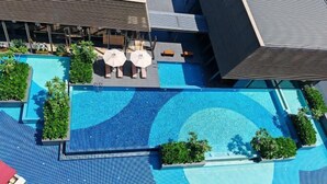 Una piscina en la azotea con sillones de descanso y sombrillas, rodeada de follaje y arquitectura moderna.