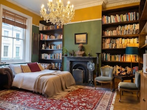 A room with a bed, a fireplace, bookshelves, a chandelier, and a window. - Burlington Palace North Wing, Palatial Suites, Velvet Dining Room, (Eastbourne)