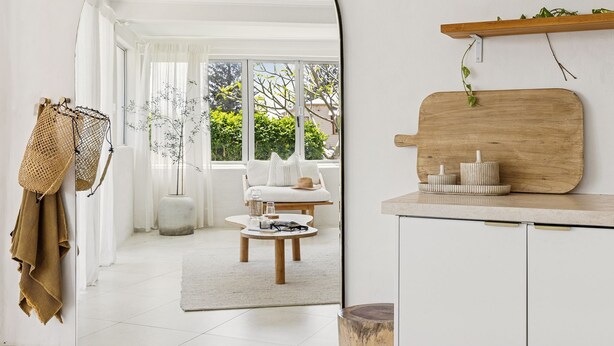 Una habitación moderna y luminosa con un ventanal grande, un sofá, una mesita y un estante de madera con adornos.