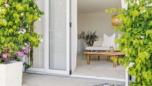 Una sala de estar moderna con un sofá, una mesa de centro y un ventanal corredera que da a un balcón con plantas.