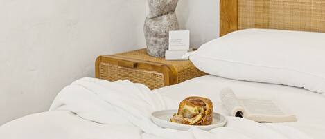 Un lit bien fait, avec des draps blancs, un livre et une assiette contenant une pâtisserie.